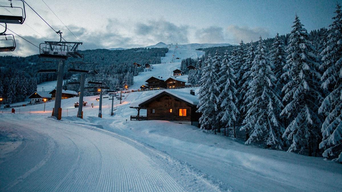 Groomed ski slope and lit chalets in an alpine village at dusk