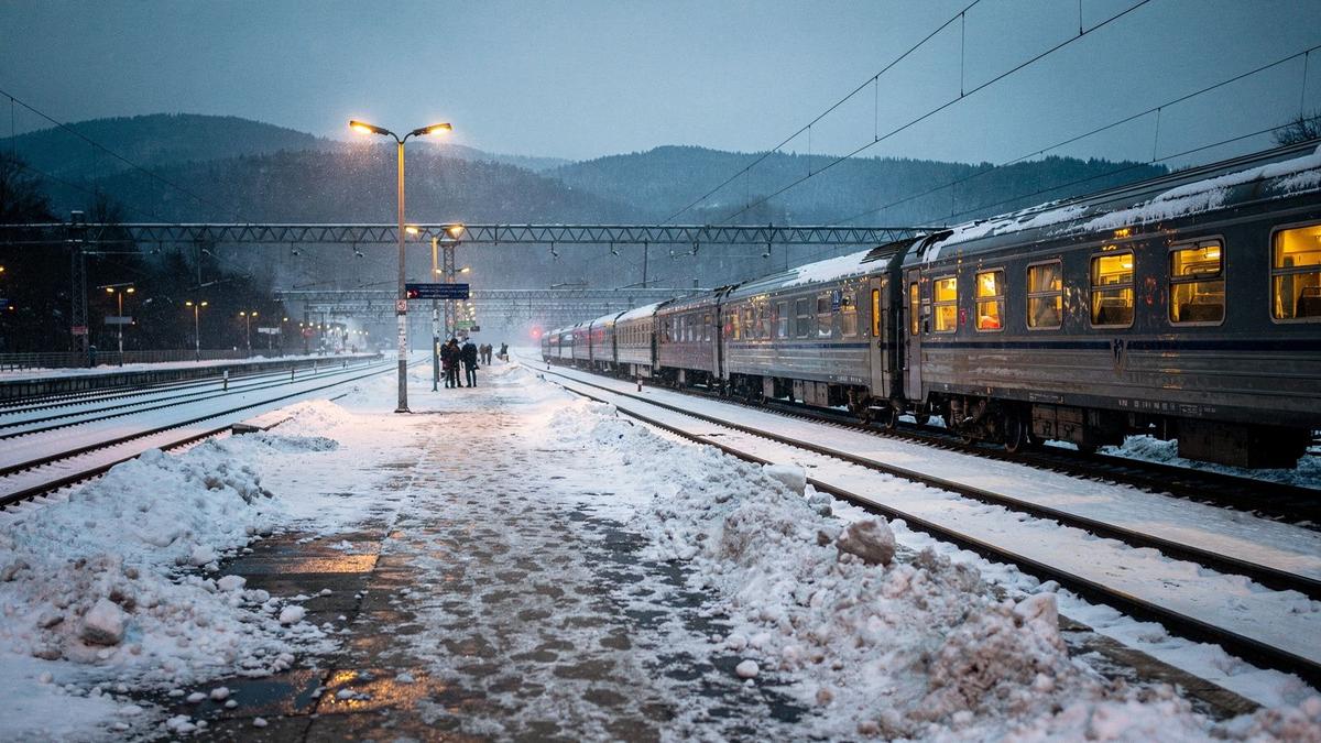 Snow-covered railway platform in the Carpathians at dusk with a waiting sleeper train